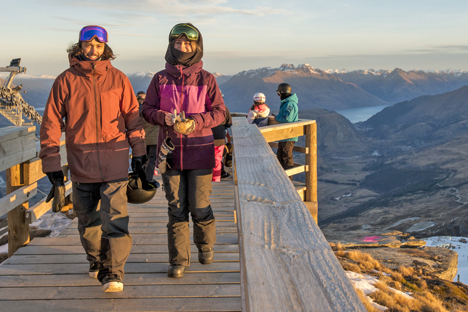 Couple walking on bridge off chairlift with mountains in the background